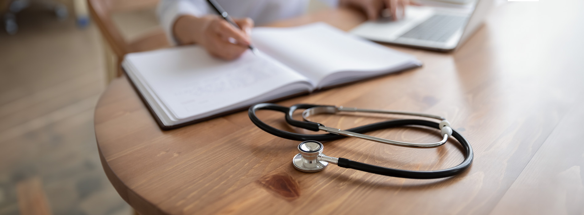 A person writing in a notebook with a stethoscope on top of it, suggesting a healthcare professional at work.